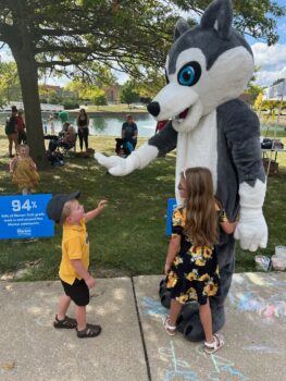 The college mascot, a giant Husky, high-fives a small boy while a girl hugs him.