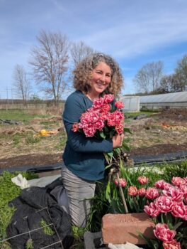 The owner, a woman with gray, curly, shoulder-length hair, cradles large pink flowers.