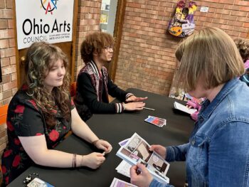 Two students talk to a shopper about their comics.