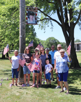 A family waves American flags in front of a military banner. 