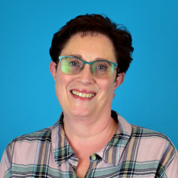A white woman with short, curly brown hair, glasses, and a smile
