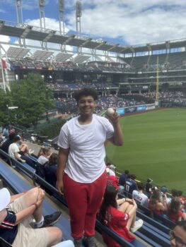 A young man smiles while holding a baseball in the stands.