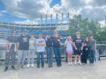 tudents stand and smile in front of the Guardians stadium.