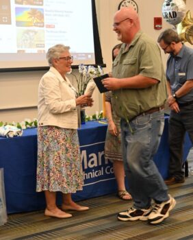 An instructor smiles at a man holding a small leather diploma.