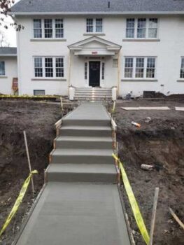 A freshly poured concrete sidewalk with stairs in front of a home.