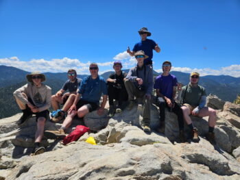 A group of Scouts and their leaders smile atop of a mountain.