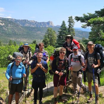 Hikers smile while wearing backpacks and holding walking sticks.