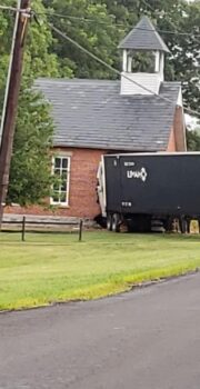 A semi-truck trailer protrudes from teh side of the brick school building.