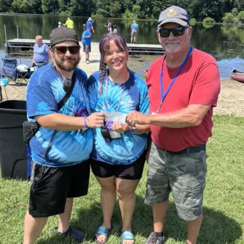 a couple in matching shirts smiles while accepting a check from a taller man.