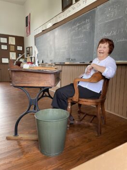 A woman smiles while sitting at the teacher's desk.
