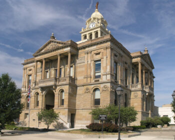 Picture of a large stone building with a huge clock tower with a dome and a statue on the top.