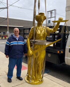 A man smiles next to a gold statue held with 