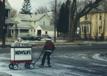 A boy in winter jacket pulls a large wagon labeled "Newslife."