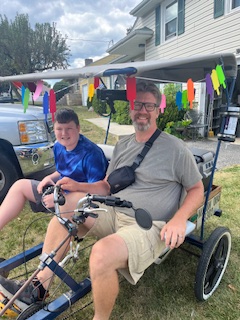 A father and son smile on the custom bike used for Jude's Chill Cycle. 