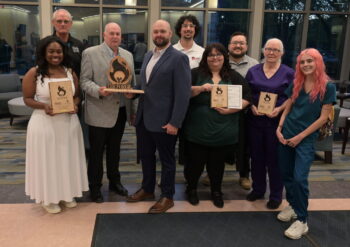 9 men and women smile while holding wooden plaques.