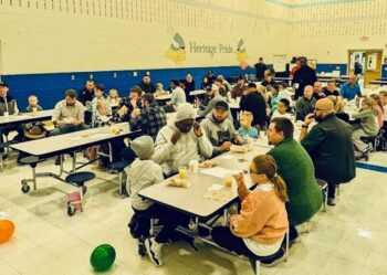 Parents and kids sit at tables enjoying donuts and juice.