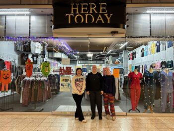 Three women smile in front of their storefront, Here Today.