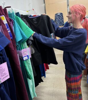 A store employee arranges scrubs on a rack