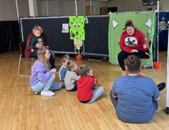 An adult reads a story to children and their mothers.