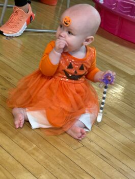 A young girl wears an orange dress with a jack-o-lantern face in a gym at a MAPP program.