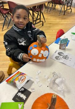 A small boy holds a pumpkin with a face made out of paper circles during a MAPP program.