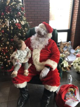 A smile child sits on Santa's lap next to a Christmas tree and gazes up at Santa during a MAPP event.