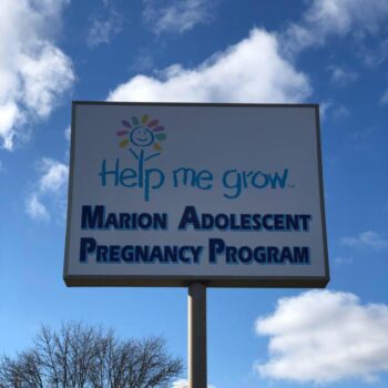 Outdoor sign under a blue side with puffy clouds stating "Help Me Grow" and "Marion Adolescent Pregnancy Program"